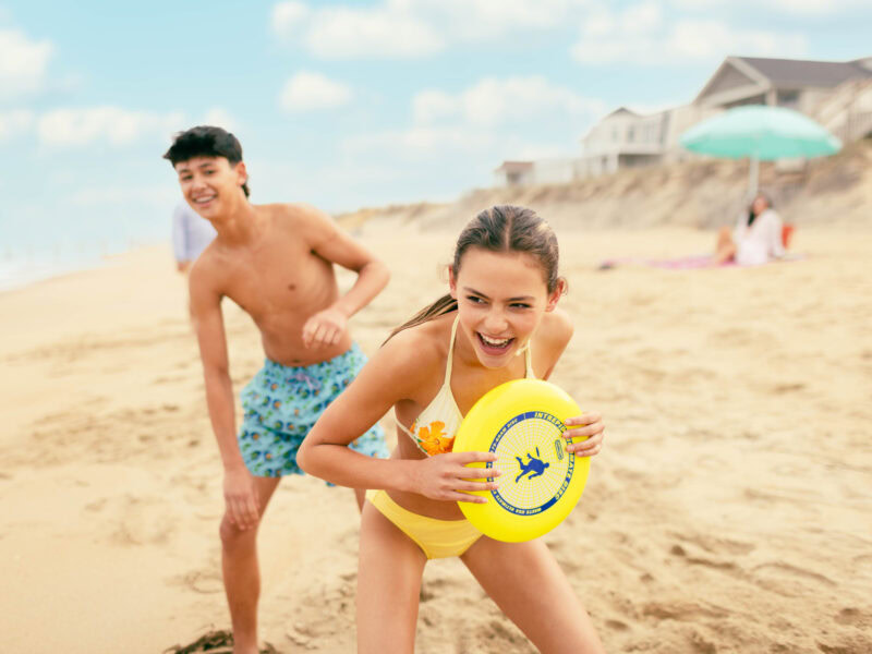 Two young friends play with a yellow frisbee on a sunny beach, smiling and enjoying summer fun.