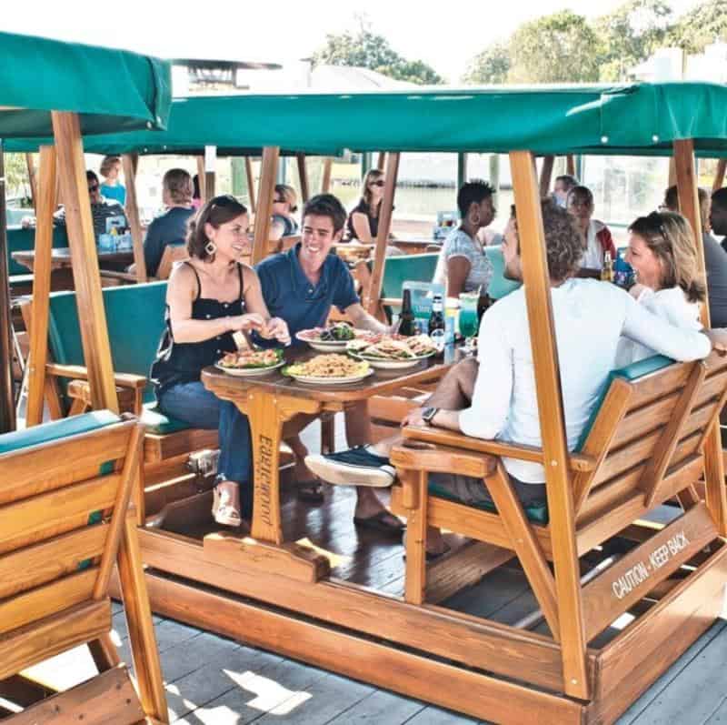 A group of people enjoying a meal at a unique outdoor restaurant with wooden seating, surrounded by a relaxed atmosphere.