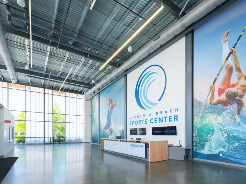 Bright and modern interior of the Virginia Beach Sports Center featuring a reception desk, large windows, and vibrant sports-themed murals.