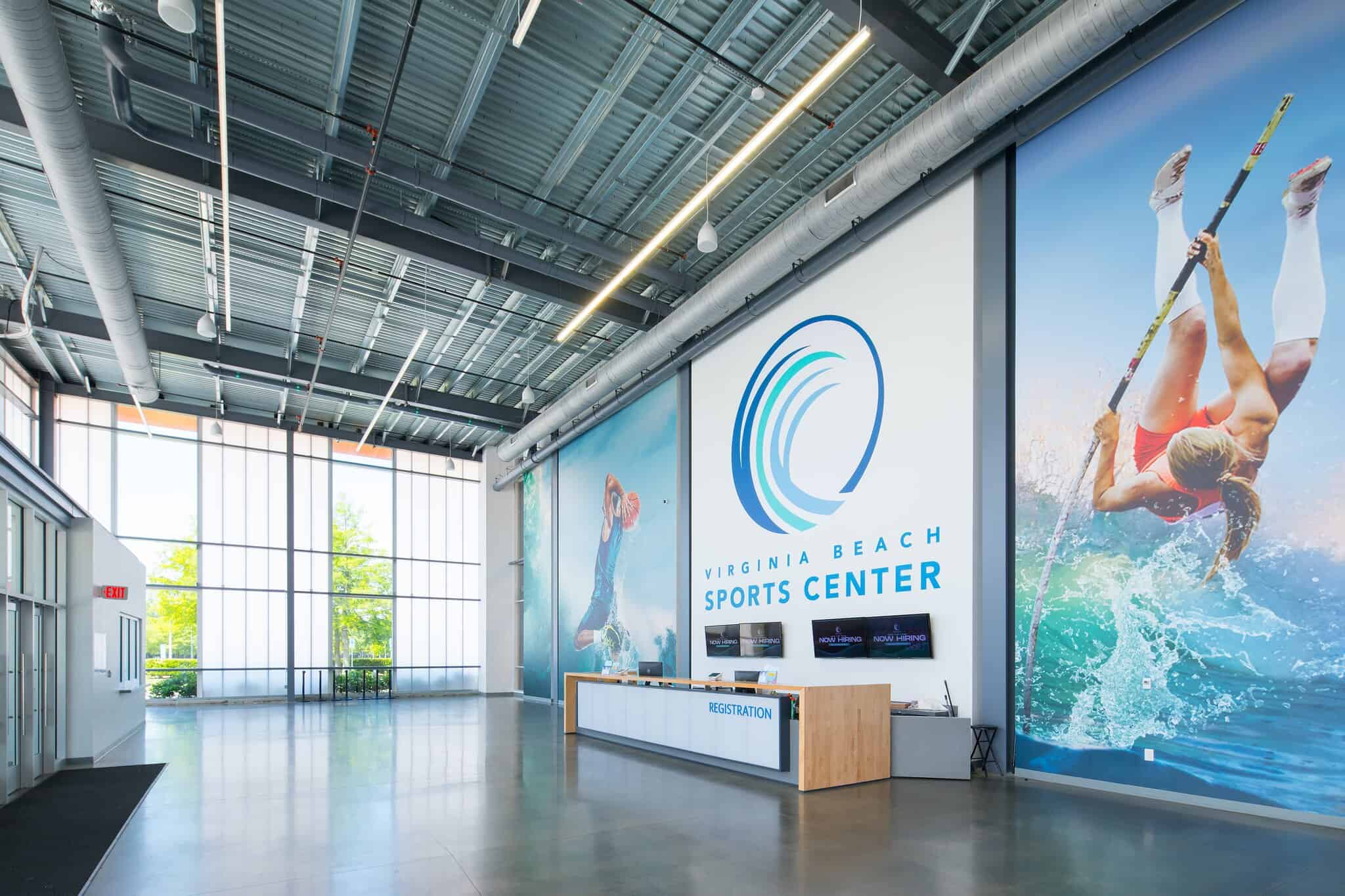 Bright and modern interior of the Virginia Beach Sports Center featuring a reception desk, large windows, and vibrant sports-themed murals.