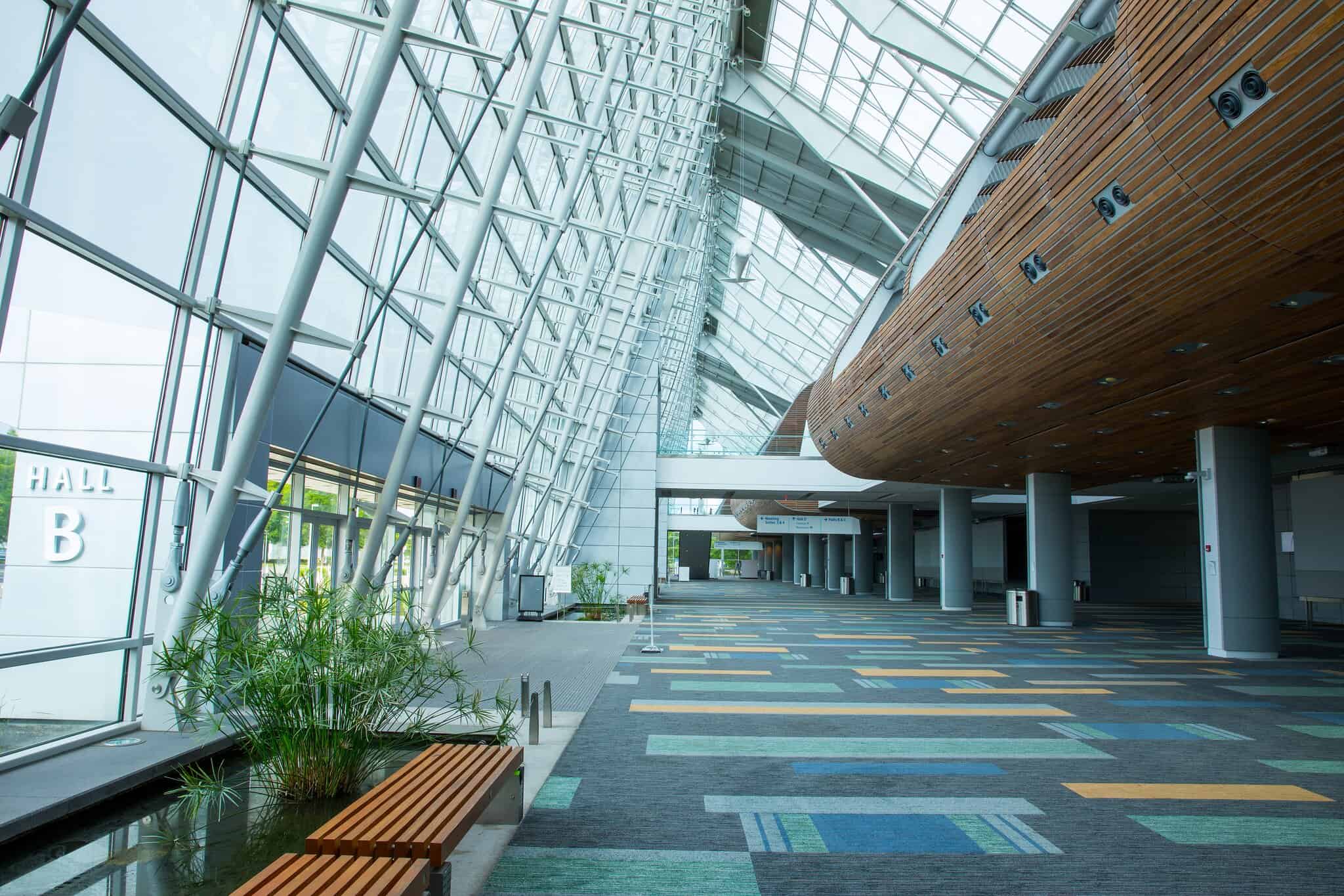 Modern airport terminal interior with large glass walls, wooden accents, and colorful carpeting.