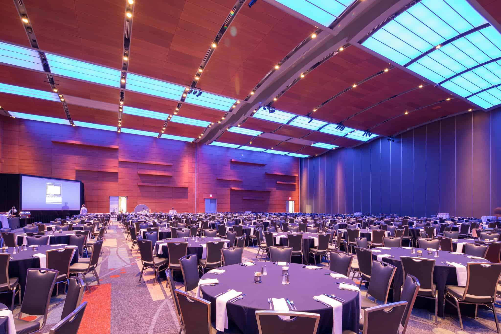 Spacious event hall set up for a banquet with numerous round tables, modern decor, and ambient lighting.