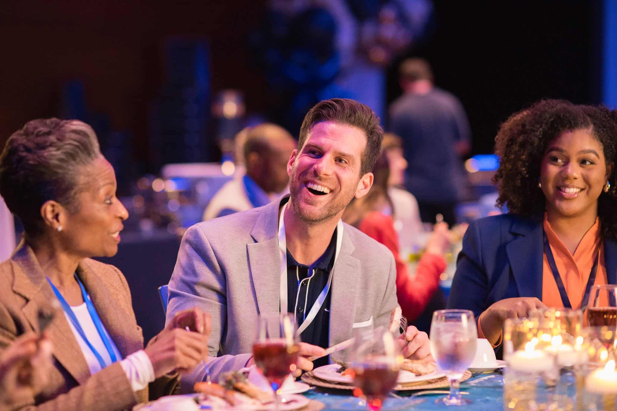 Diverse group of people enjoying dinner at a formal event, with smiling individuals engaging in lively conversation.