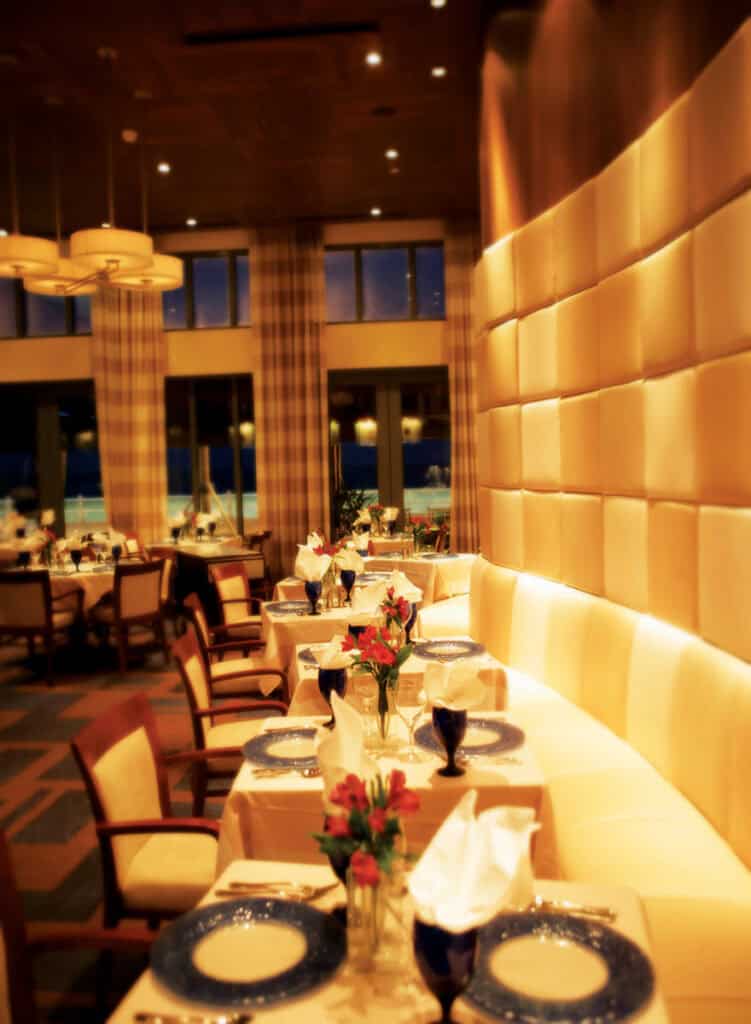 Elegant restaurant interior featuring tables set with blue dinnerware, floral centerpieces, and warm ambient lighting.