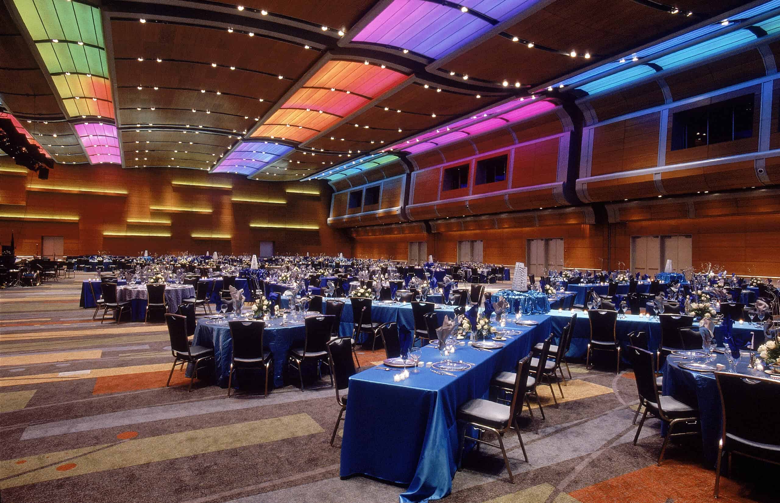 Elegant banquet hall with blue table settings and colorful lighting, prepared for a large event or celebration.