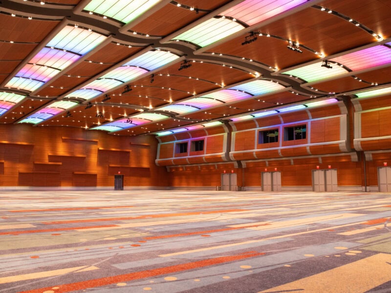 A spacious and modern event hall featuring colorful LED lighting, wooden walls, and patterned carpeting, ideal for gatherings.