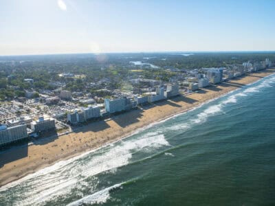 Aerial view of a beach with high-rise buildings along the shore, showcasing sandy beaches and ocean waves under a clear sky.