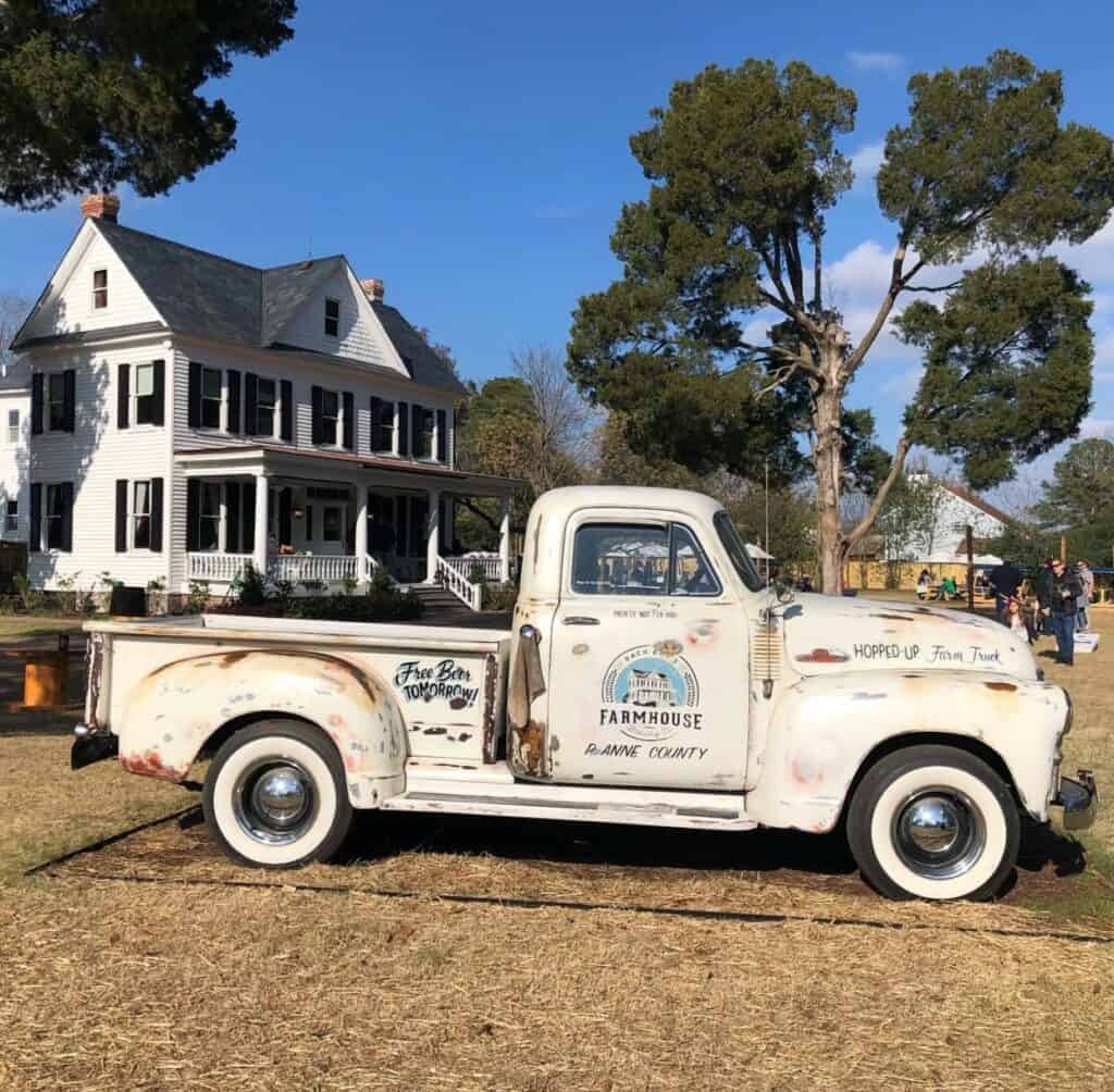Rustic vintage truck parked in front of a white farmhouse with a blue sky, featuring phrases like "Free Bar Tomorrow" and "Farmhouse."
