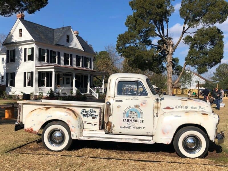 Rustic vintage truck parked in front of a white farmhouse with a blue sky, featuring phrases like 