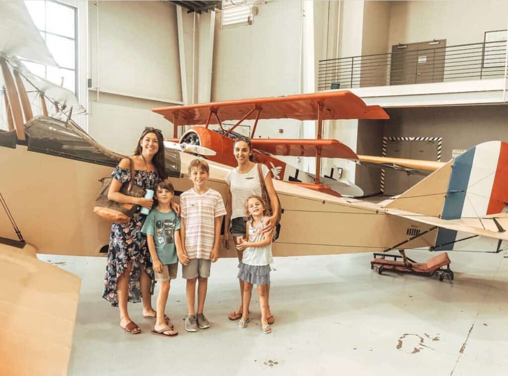A family poses with a vintage biplane at the Military Aviation Museum, enjoying their visit with smiles and casual attire.