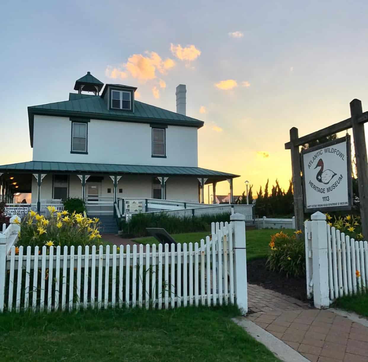 Atlantic Wildfowl Heritage Museum building at sunset, featuring a white fence and vibrant yellow flowers in the foreground.