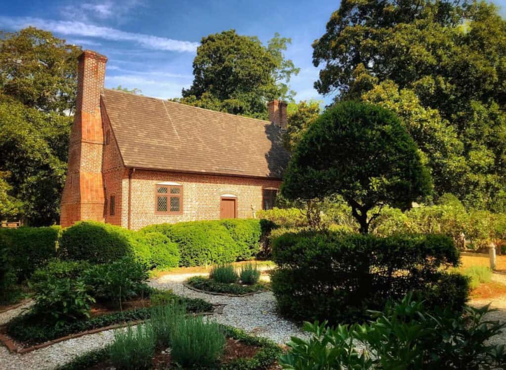 The historic Adam Thoroughgood House surrounded by lush gardens and well-maintained hedges under a clear blue sky.