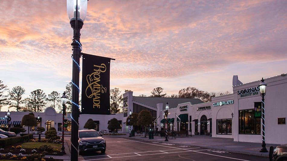 Scenic view of a shopping promenade at dusk, featuring storefronts like Savarnas Beauty Spa and Club Pilates, under a colorful sky.