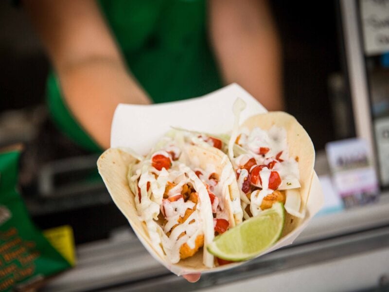 Tacos filled with fried fish, shredded cabbage, and diced tomatoes, topped with a creamy sauce and served with a wedge of lime at Bro's Fish Taco Food Truck.