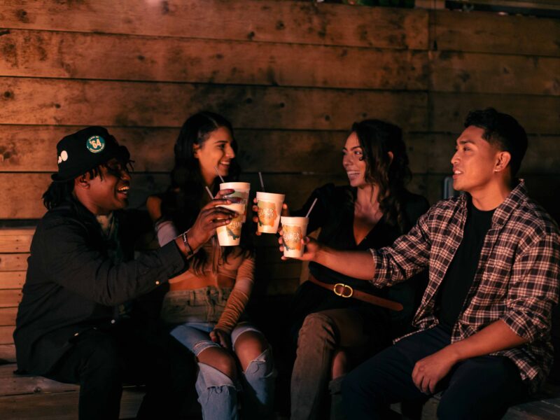 A group of four friends enjoys drinks together, celebrating and laughing in a cozy, dimly-lit outdoor setting at The Shack in Virginia Beach.