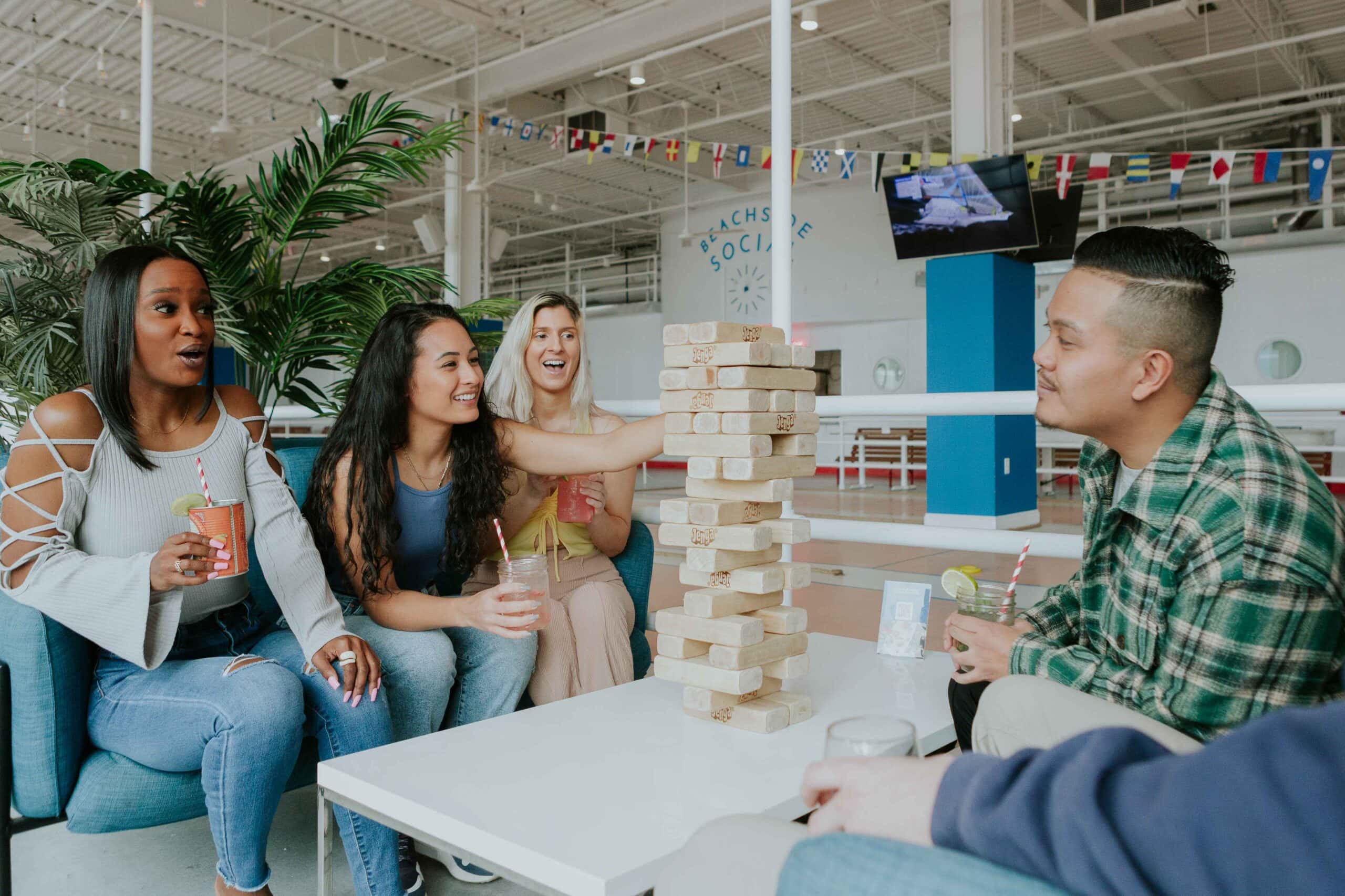 A group of friends enjoys drinks while playing Jenga in a lively social setting, surrounded by greenery and vibrant decor at Beachside Social.