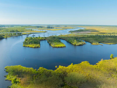 Aerial view of a serene wetland landscape in Pungo featuring winding rivers, small islands with greenery, and Pungo Ferry Bridge crossing the waterways.