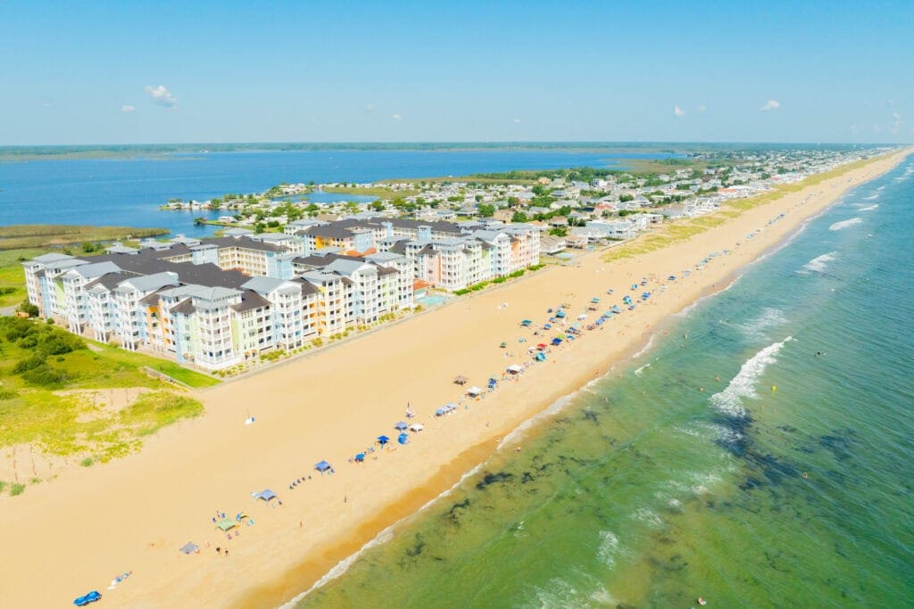 Aerial view of Sandbridge Beach, a sandy beach with colorful beachfront apartments, umbrellas, and waves, showcasing a vibrant coastal atmosphere in Virginia Beach.