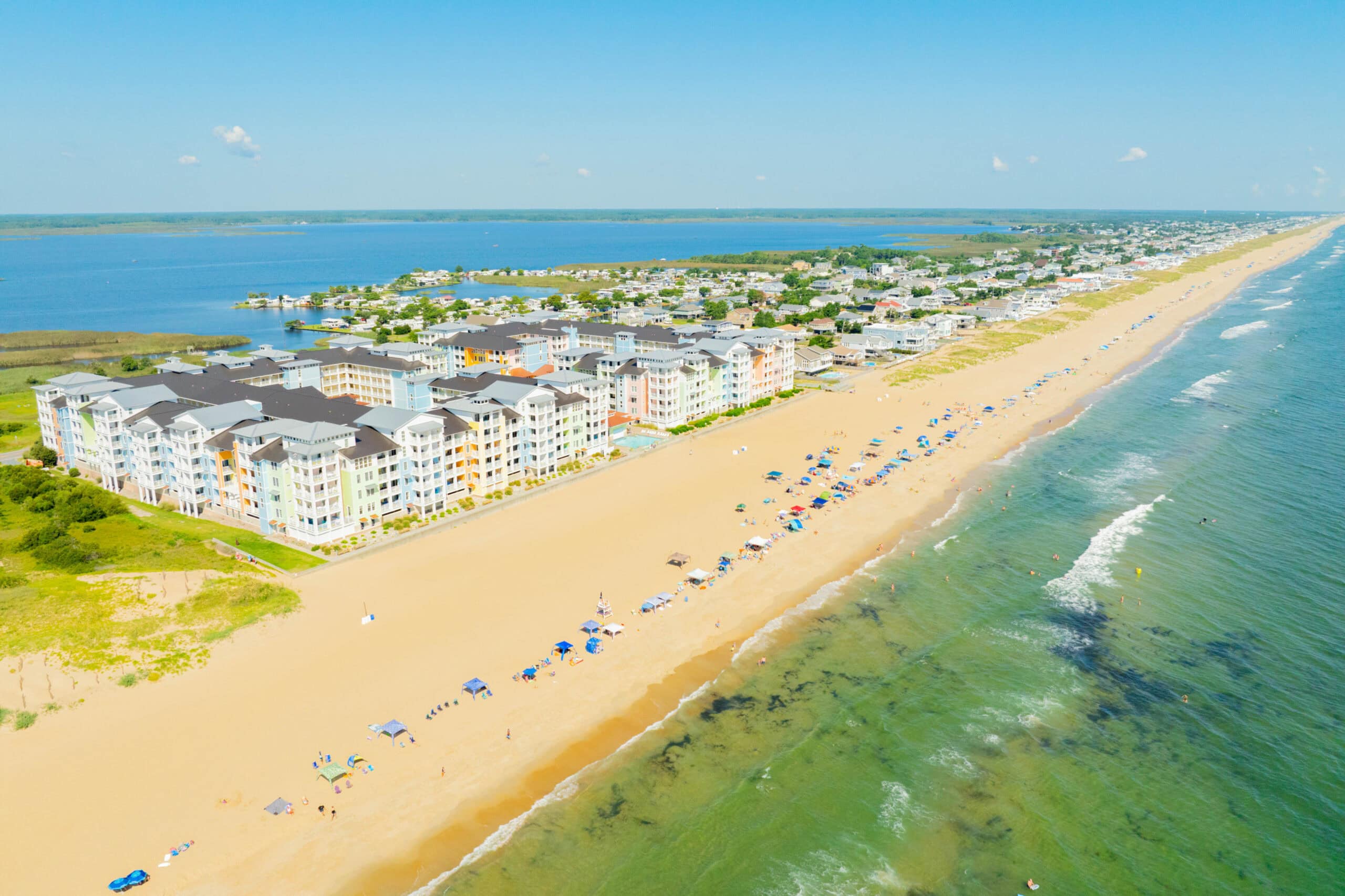 Aerial view of Sandbridge Beach, a sandy beach with colorful beachfront apartments, umbrellas, and waves, showcasing a vibrant coastal atmosphere in Virginia Beach.