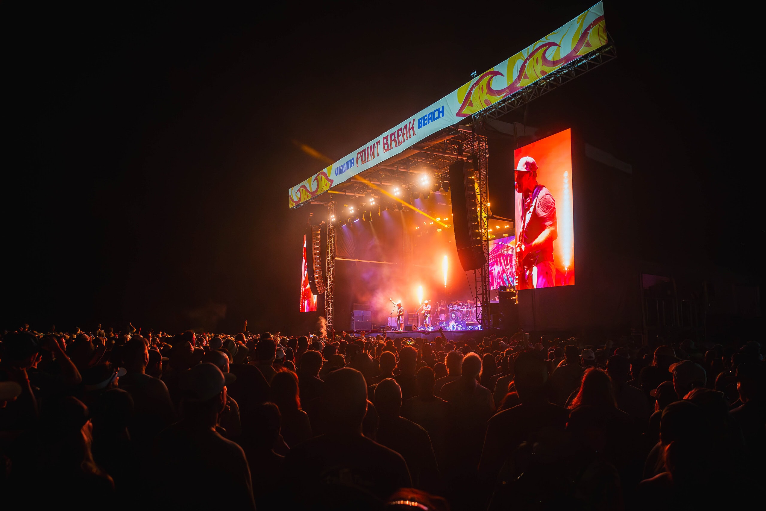 A large crowd at Point Break Music Festival during night time with vibrant red light cast on them in Virginia Beach