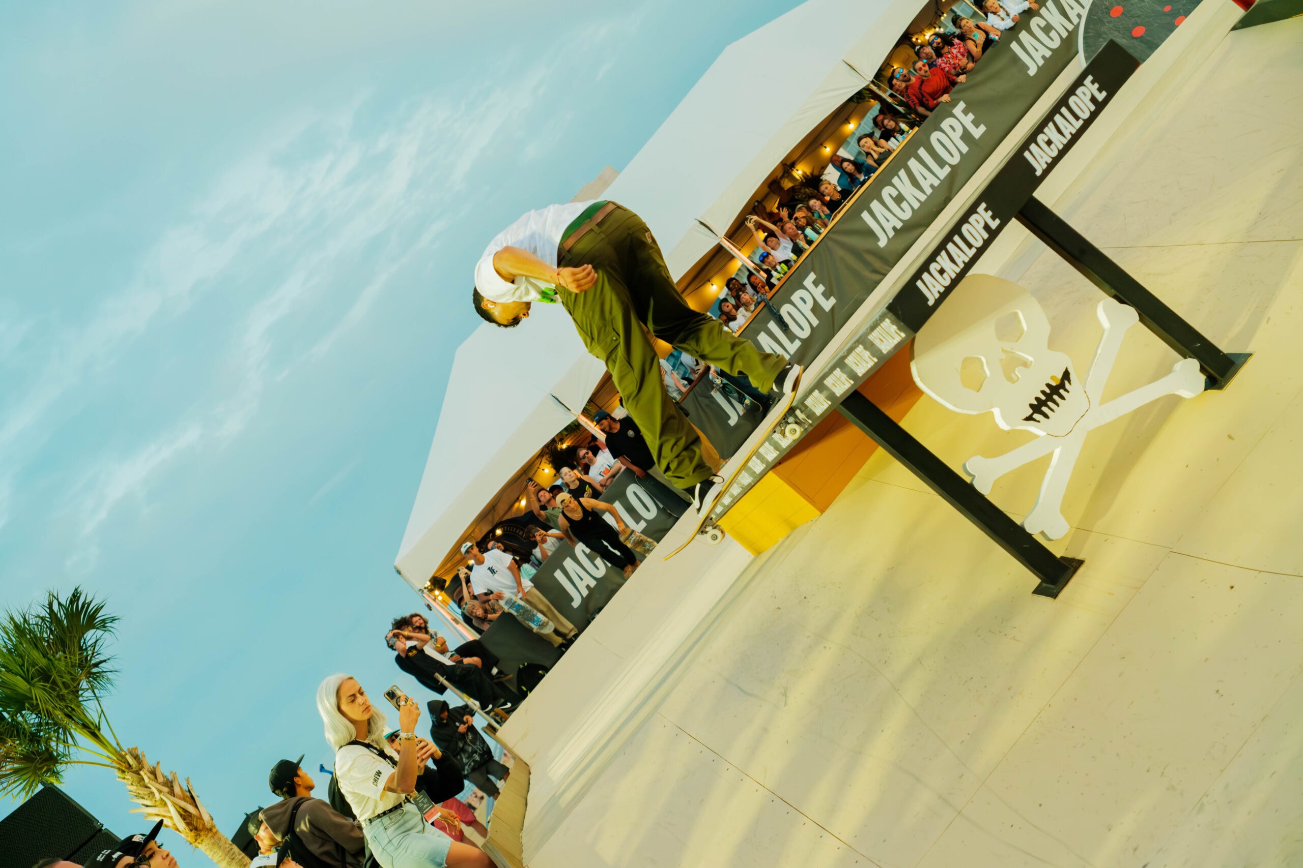 A skateboarder performs a trick on a rail at Jackalope Festival an outdoor event, with an audience and tents in the background.
