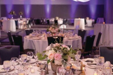 Elegant banquet setup featuring round tables adorned with floral arrangements, candles, and glassware.