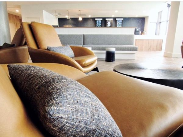 Two brown leather chairs are in the foreground with a dark coffee table and a grey couch in the background at Delta Virginia Beach Bayfront Lobby.