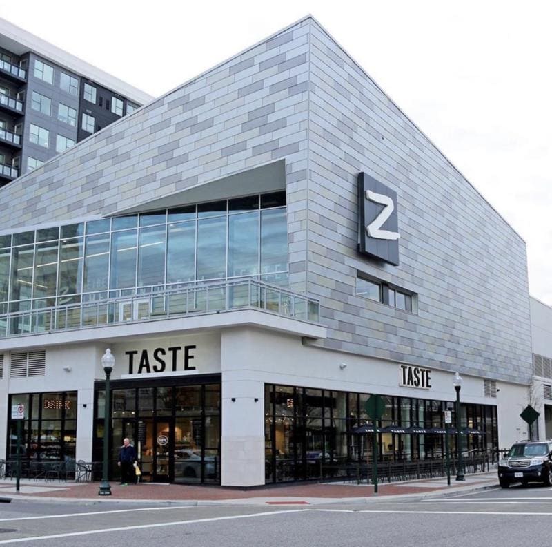 A corner of a street is depicted from Town Center with brick buildings lining the street while one building has a sign which has a logo containing the letter "Z," for Zeiders American Dream Theater