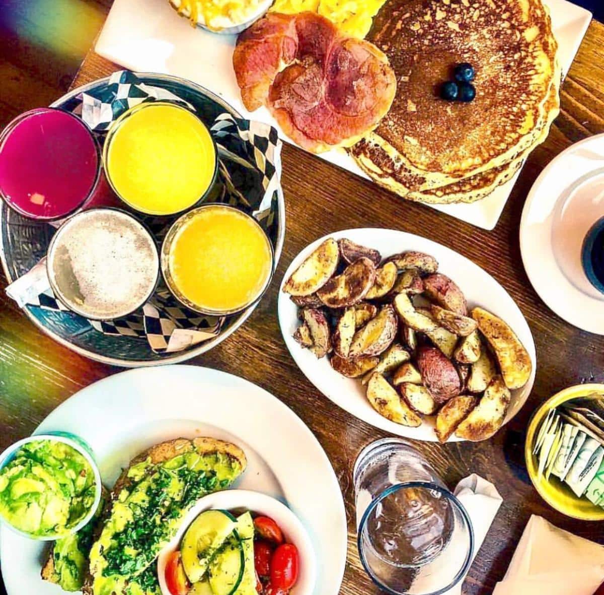 An aerial view of a table with plates of scrumptious looking food and colorful drinks at The Bee & the Biscuit restaurant.
