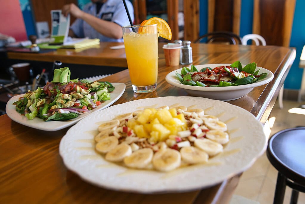A table with two plates of nicely prepared salad and a plate of fruit beautifully displayed served with an Orange Crush garnished with orange slices at Java Surf.