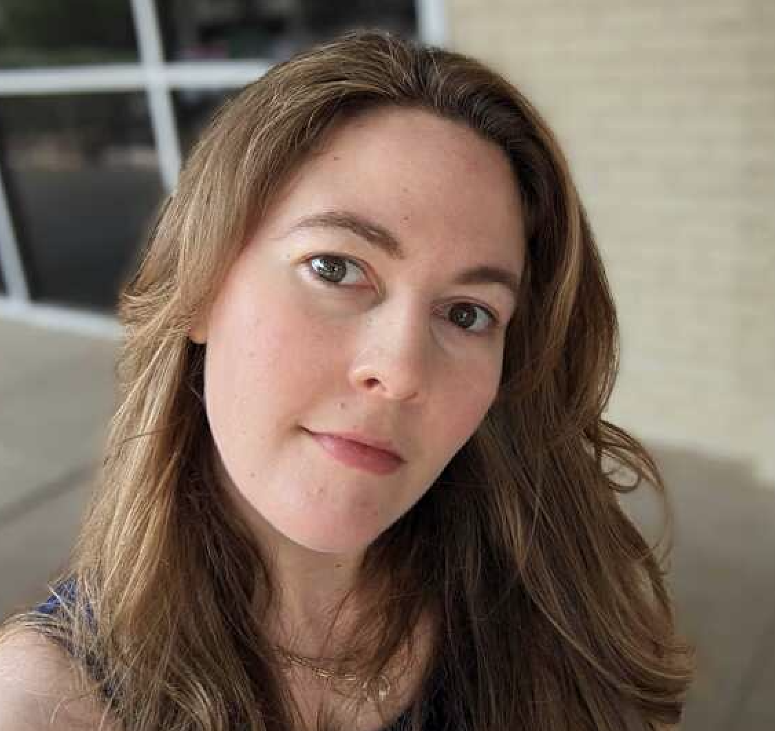 Author A woman with long light brown hair looks at the camera with a neutral expression, standing outside near a beige wall and large window.