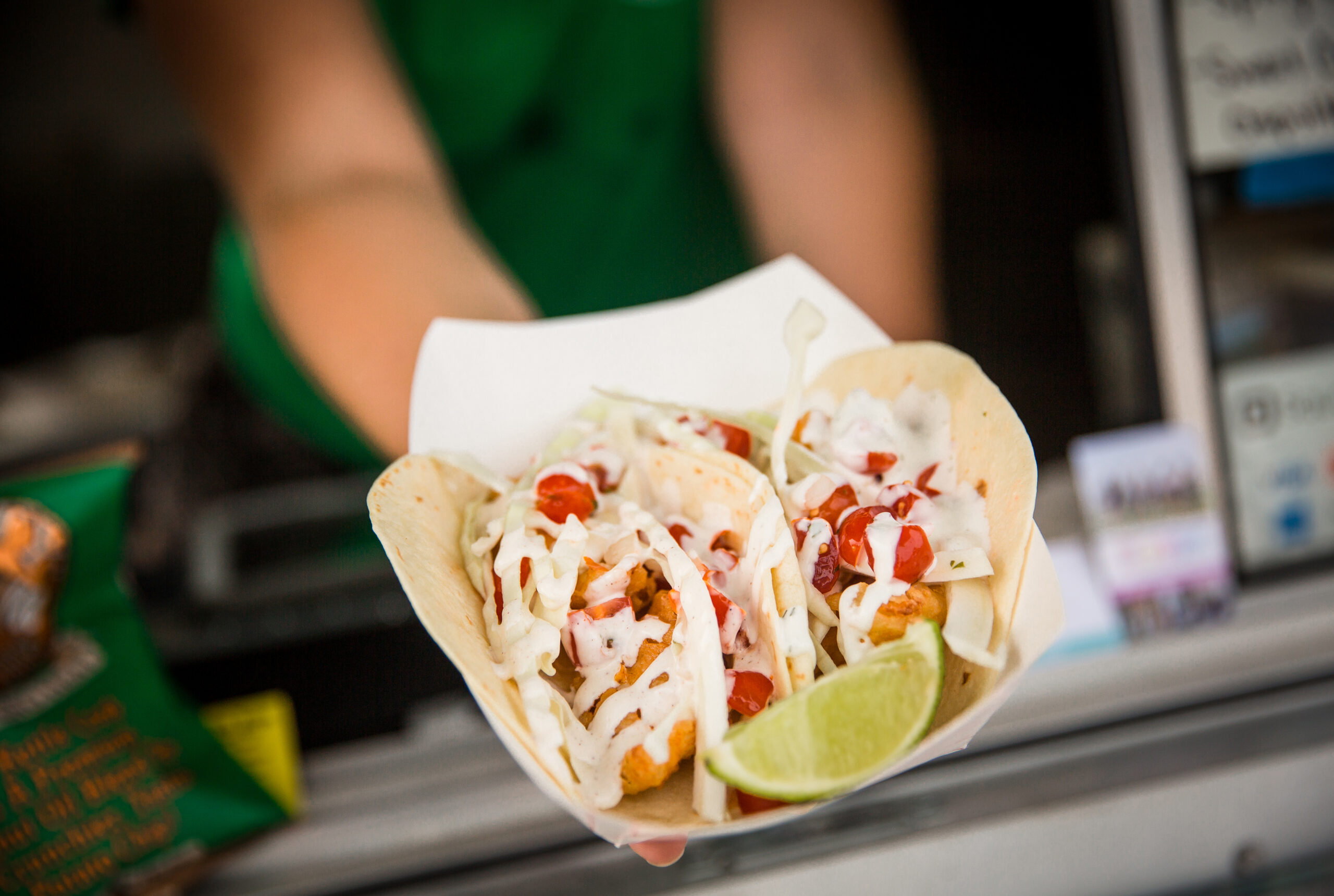 Tacos filled with fried fish, shredded cabbage, and diced tomatoes, topped with a creamy sauce and served with a wedge of lime at Bro's Fish Taco Food Truck.
