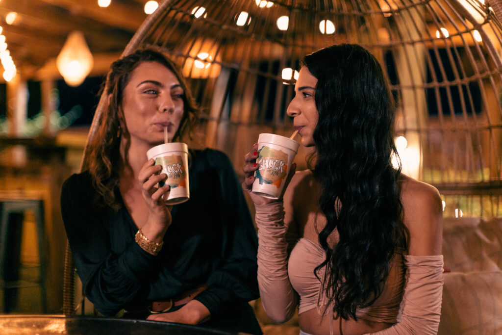 Two girl friends enjoying orange crush drinks from The Shack at night with hanging lights in the background.