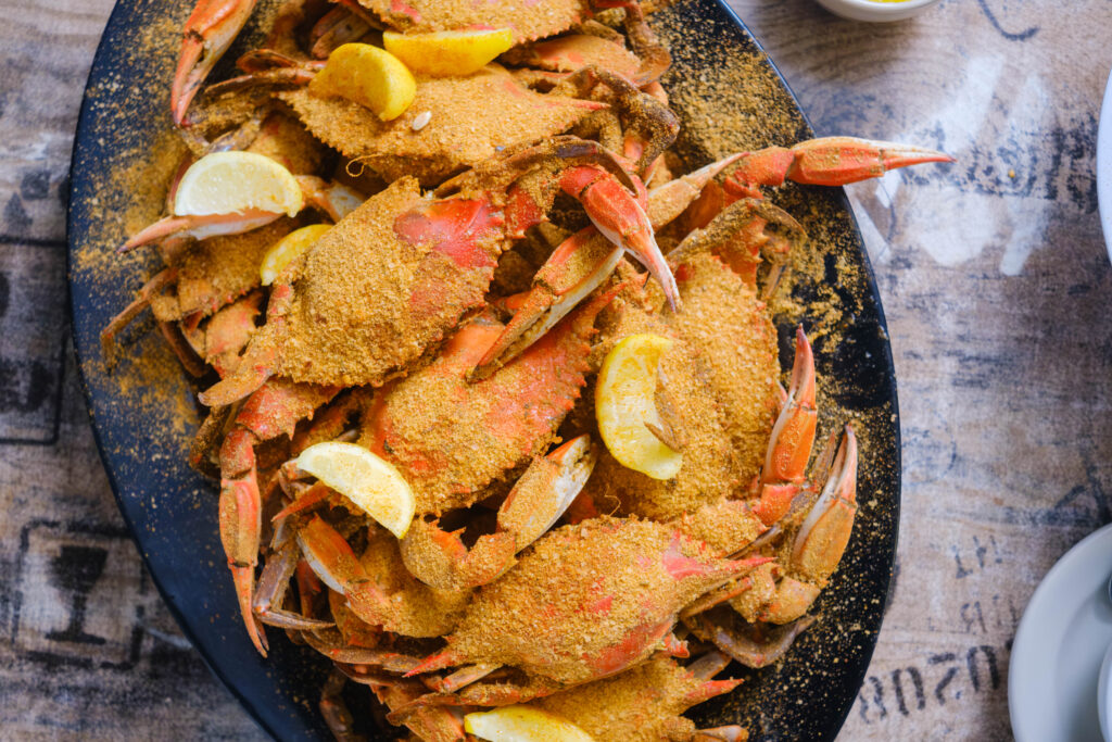 A plate of mixed seafood with crabs, shrimp, and clams on a wooden table by a poolside.