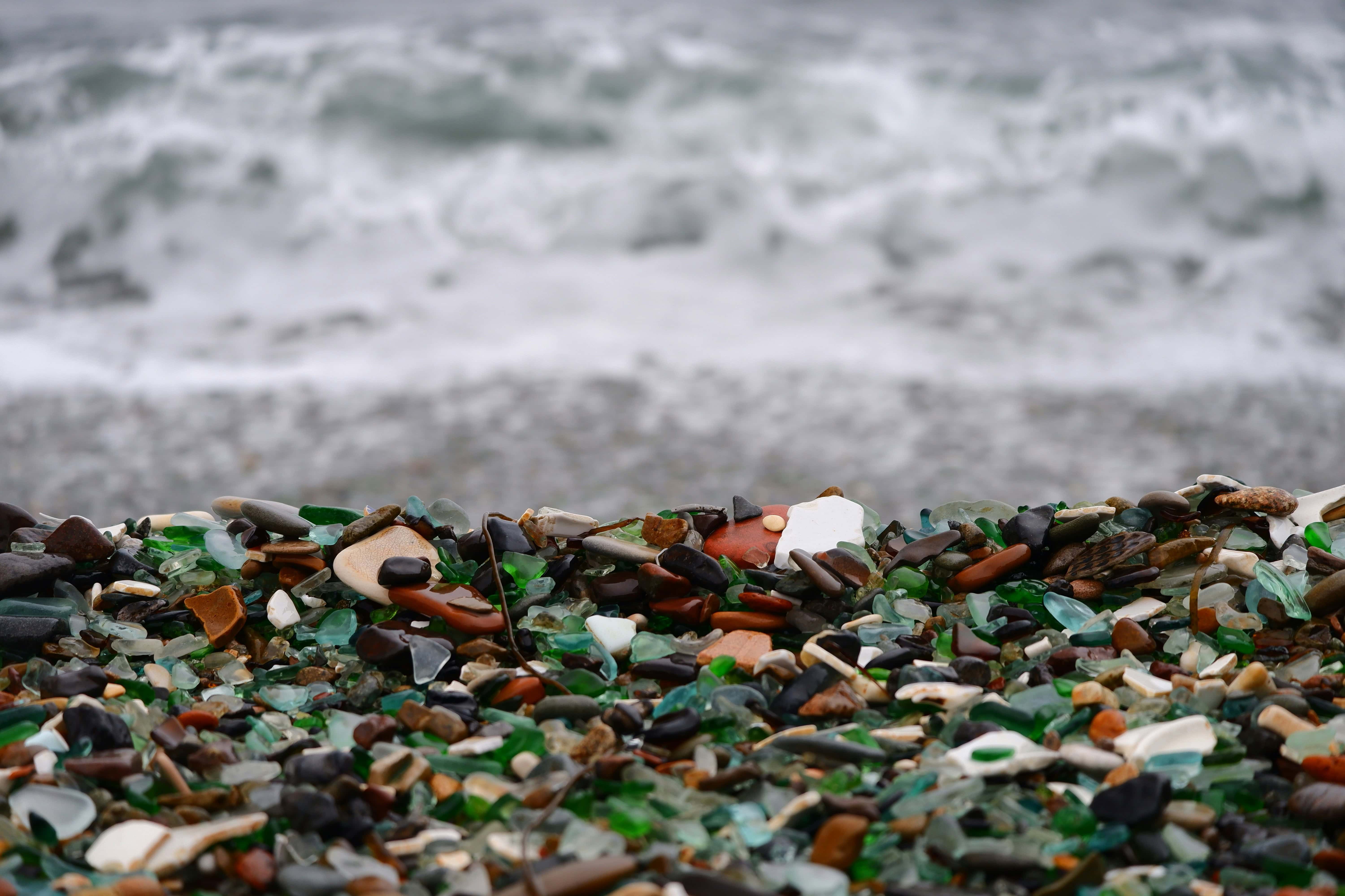 With a gloomy ocean in the background, a cluster of blue, green, and brown seaglass takes the forefront of the image.