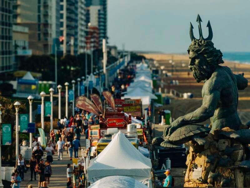 King Neptune statue overlooking crowds and festival vendors along the Virginia Beach Boardwalk during Neptune Festival.